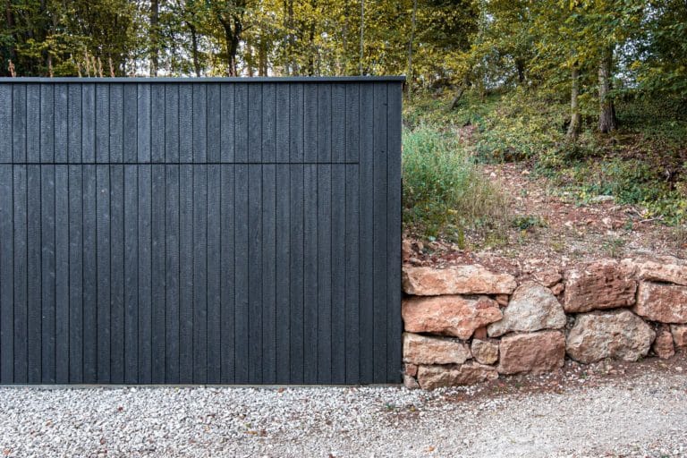 Black wooden garage in front of trees