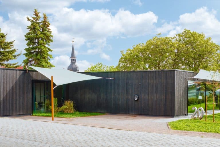 Black wooden house with church and trees in background against a blue sky