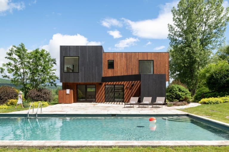 House with a black and light brown facade and a large pool in the front